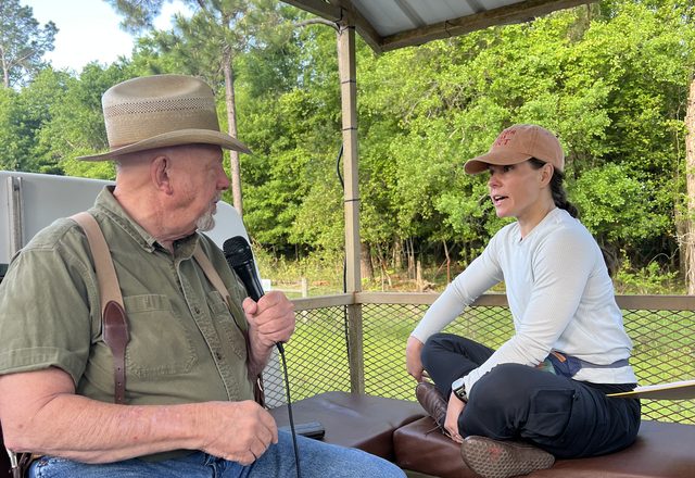 Jessi listening to a farmer holding a microphone, seated under a shelter on his land