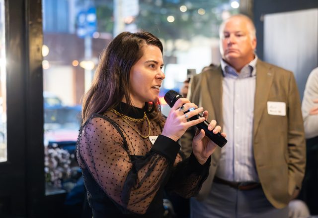 Jessi speaking into a handheld microphone at an evening event