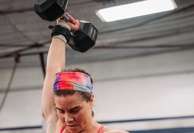Jessi pressing a dumbbell overhead in a gym
