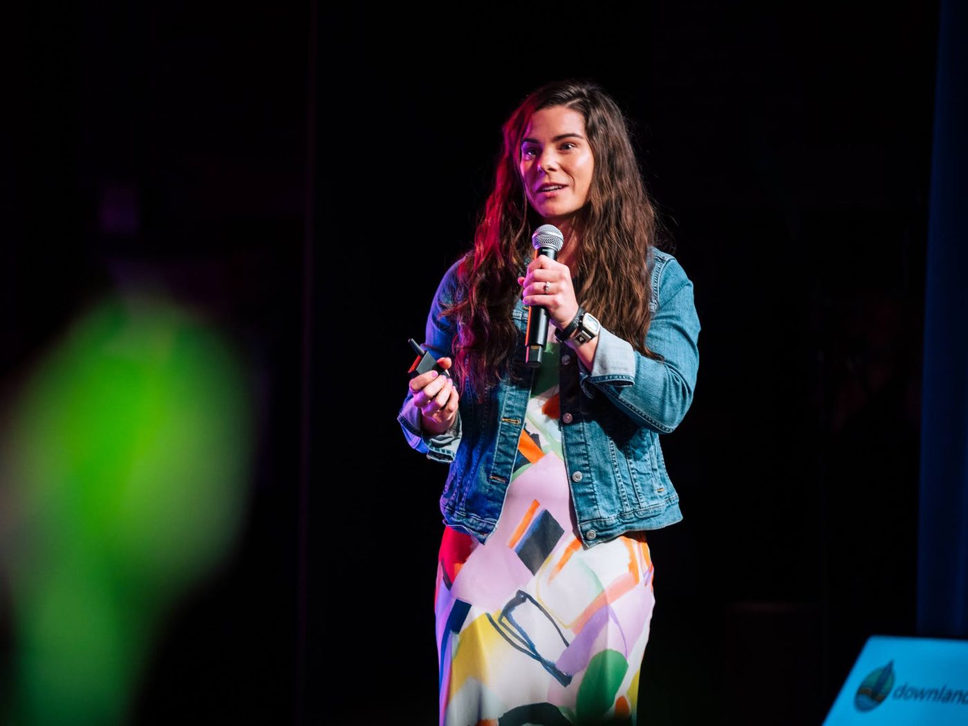 Jessi speaking on stage with a microphone in a denim jacket