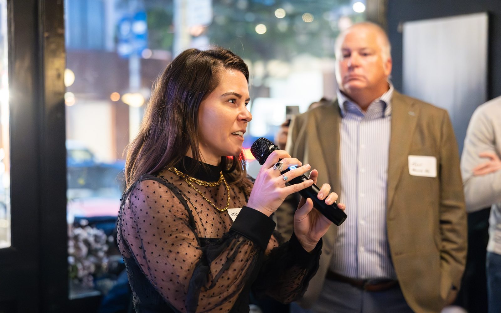 Jessi speaking into a handheld microphone at an evening event